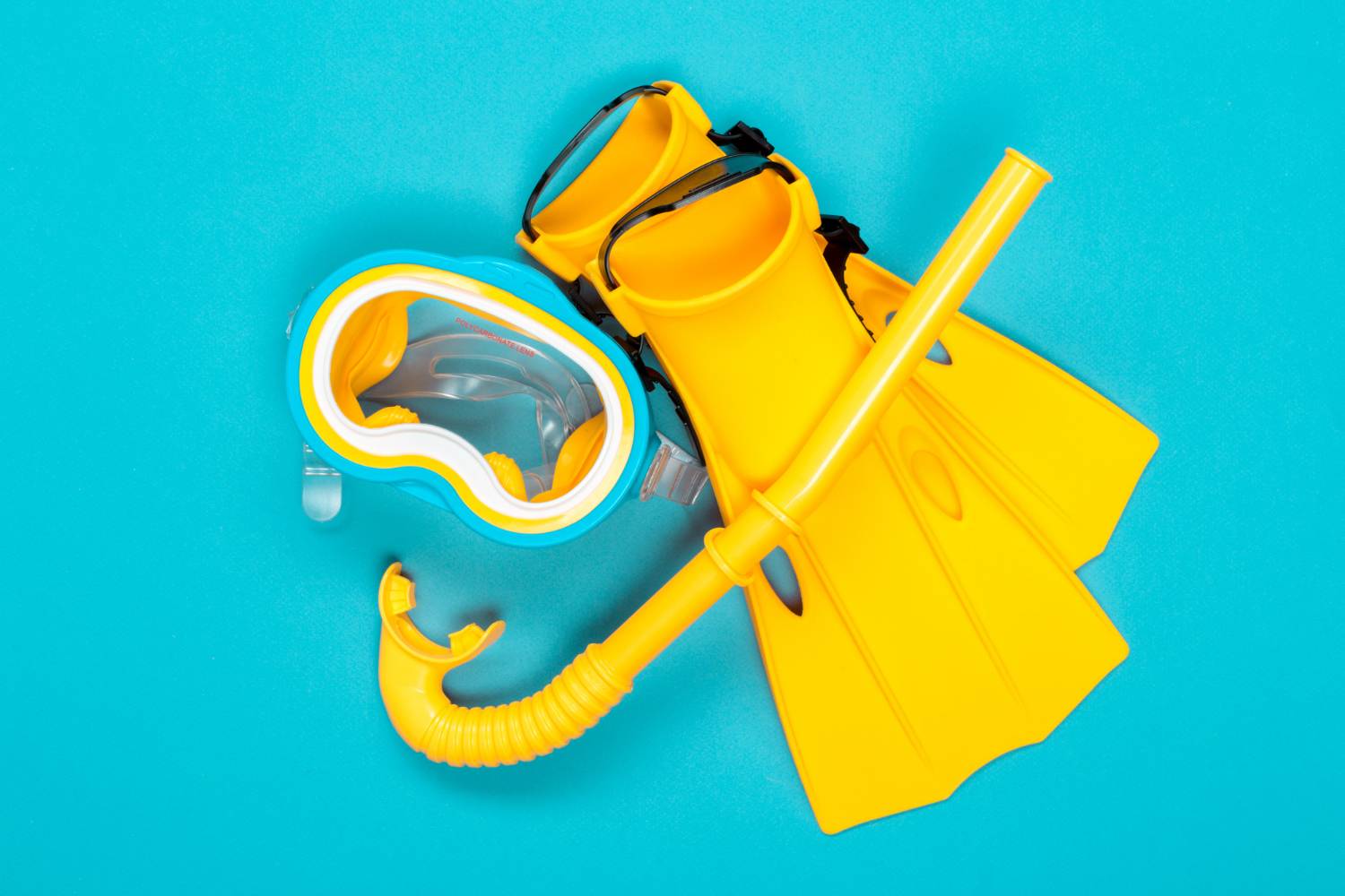 Yellow snorkel gear, including a mask, fins, and snorkel, arranged on a bright turquoise background. Day trip to Shell Island essentials.