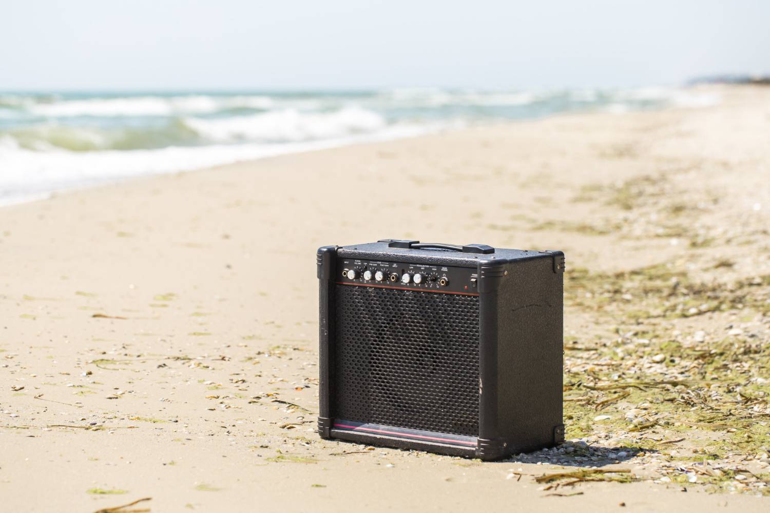 A black amplifier sits on a sandy beach near the ocean waves, ideal for amplifying the ultimate pontoon boat playlist for a fun-filled day.