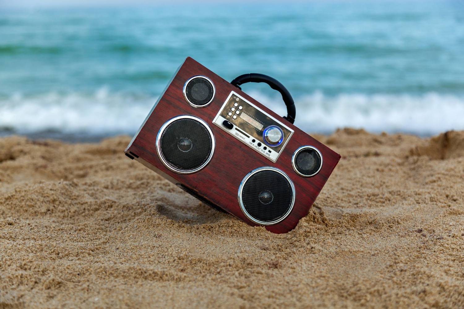 Music and WaveA vintage boombox rests on sandy beach with the ocean waves in the background, perfect for creating the ultimate pontoon boat playlist.s