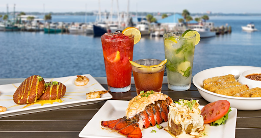 A table with delicious seafood dishes and colorful drinks, with a view of boats docked in the marina and the bay in the background. Uncle Ernie's in Panama City.